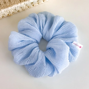 Detailed close-up of sky blue pleated scrunchie with handmade woven label detail