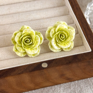 Gros plan de boucles d'oreilles roses en résine verte avec pétales dans un écrin en bois