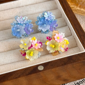 Détail de boucles d'oreilles fleuries faites main avec perles en tons bleus et jaunes