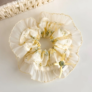 Détail d'un chouchou floral avec bordure en dentelle, nœud jaune et étiquette faite main