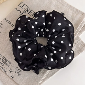 Close-up of black satin scrunchie with white polka dots on a rustic linen background
