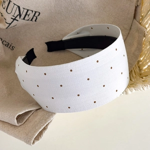 Detail view of the white wide headband with brown polka dots on a linen fabric background