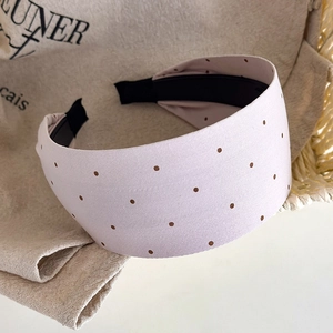 Detailed view of pink polka dot headband placed on rustic beige linen and rattan