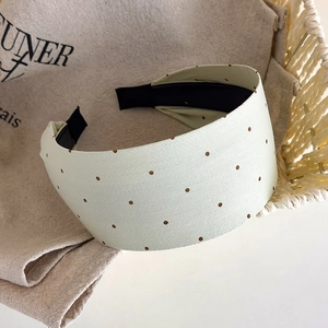 Detail view of light green polka dot headband on a beige textured cotton bag