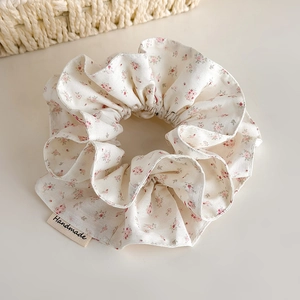 Detail of floral scrunchie with handmade tag on beige surface with woven basket