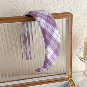 Detail view of purple plaid sponge headband on glass box with aesthetic warm lighting
