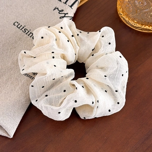 Detailed macro of white chiffon polka dot hair scrunchie on a rustic wooden table