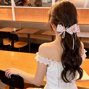Pink polka dot bow hair clip with flowing ribbons shown on model in cafe setting