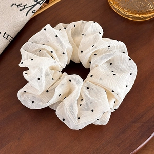 Detail of cream pleated chiffon scrunchie with black polka dots on wooden surface