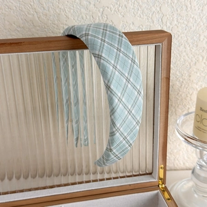 Close-up of a wide padded light green plaid headband on a wooden jewelry box