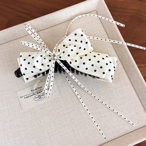 Detail view of cream satin bow hair clip with black polka dots and centered rhinestone