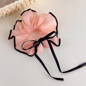Detailed shot of a pink mesh scrunchie featuring black wavy edges and a delicate ribbon bow