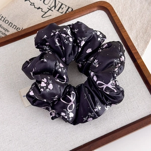 Dettaglio di scrunchie in raso nero con fiori rosa e motivi a fiocco eleganti
