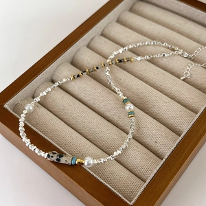 Détail d'un collier de perles et pierres vertes sur un présentoir à bijoux en velours chic