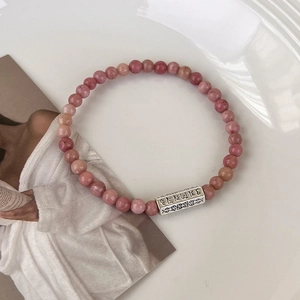 Gros plan de perles en pierre naturelle rose et charme rectangulaire aux motifs tibétains