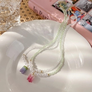 Dettaglio di collane con tulipano, perle e perline verdi su vassoio in ceramica bianca