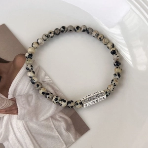 Gros plan d'un bracelet en perles de pierre avec charme en métal argenté et gravure tibétaine