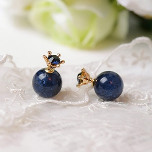 Detalle de pendientes vintage de corona dorada con cuentas azules sobre tela de encaje