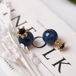 Detalle de pendientes de corona con cuentas de mármol azul y baño de oro en una revista