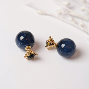 Detalle macro de pendientes de perla azul estrellada con corona dorada y cristal negro