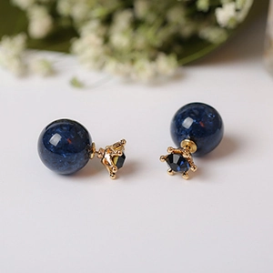 Detalle de pendientes esféricos azules con textura de mármol y base de corona dorada