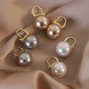 Detailed close-up of champagne, grey, and pink pearl hoop earrings on satin fabric
