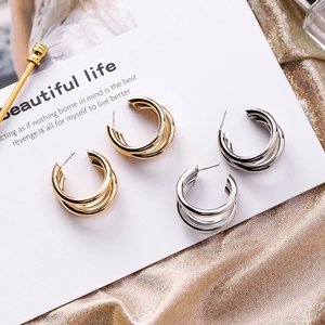 Close-up of triple-layered gold and silver C-shaped hoop earrings on a decorative card