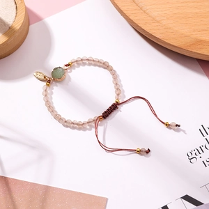 Detail of pink beaded bracelet featuring a raw green stone pendant and woven cord