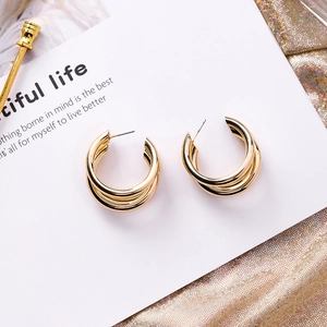 Macro detail of triple-layered gold-plated geometric C-shape hoop earrings on a card