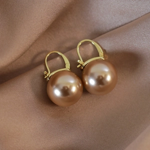 Detail of champagne pearl earrings on brown silk fabric with golden metal hooks