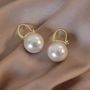 Detail of champagne pearl drop earrings on champagne silk background in warm lighting