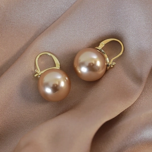 Close-up of champagne pearl earrings on elegant matching satin fabric background