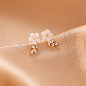 Macro detail of shell flower stud earrings with marquise zircon leaves on champagne silk