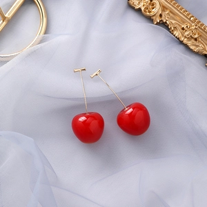 Vue macro de boucles d'oreilles cerises rouges avec crochets dorés sur tulle bleu clair