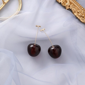 Détail de boucles d'oreilles cerises en résine rouge et tiges dorées sur fond de gaze