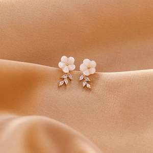 Detailed close-up of shell flower earrings with gold leaf and teardrop zircon accents