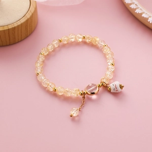 Detailaufnahme des Perlenarmbands mit süßem weißen Katzenanhänger und goldenen Akzenten
