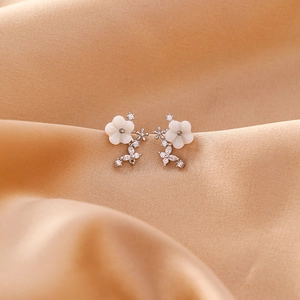 Macro shot of silver flower and butterfly stud earrings on beige silk fabric
