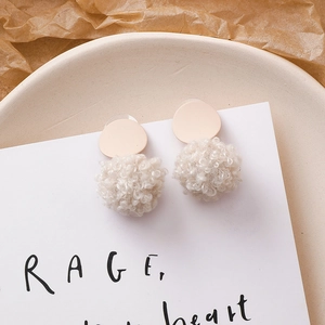 Détail de boucles d'oreilles pompon beige en texture laine d'agneau douce pour l'hiver