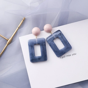 Close-up of geometric blue marble earrings with pink resin studs on white cardstock