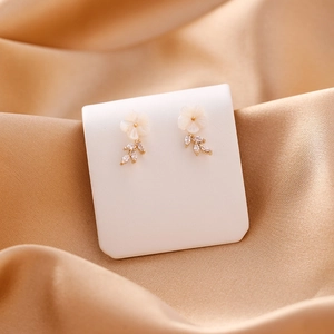 Detail view of shell flower earrings with marquise zircon drops on a soft satin fabric