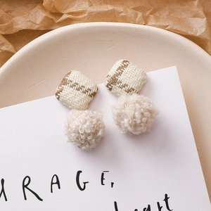Détail de boucles d'oreilles d'hiver avec pompons beiges et textures de tissu tissé