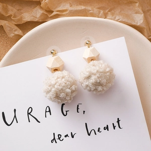 Détail de boucles d'oreilles d'hiver avec pompons en fourrure crème, perles bois et métal doré