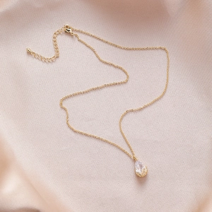 Close-up of golden teardrop zircon necklace on champagne silk background