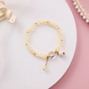 Detail eines Perlenarmbands mit gelben Kristallen und weißem Keramik-Glückskatzen-Anhänger