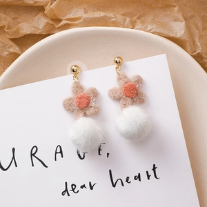 Détail de boucles d'oreilles d'hiver avec fleurs en feutre et pompons blancs sur carte