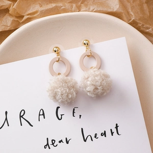 Détail de boucles d'oreilles boules en peluche beige avec clous dorés et anneaux résine