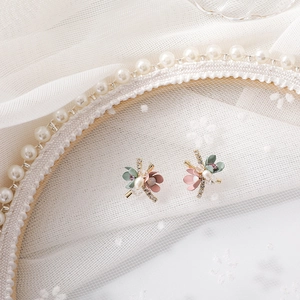 Macro shot of floral stud earrings with pink petals, pearls, and crystals on white lace