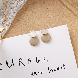 Détail de boucles d'oreilles rondes beige et blanc avec bordure dorée sur carte