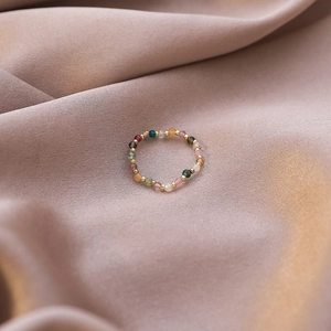 Macro detail of multi-colored beaded stretch ring on elegant soft pink satin background